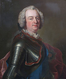 Oil portrait of a man from the waist up. He has a pale complexion and rosy cheeks, with a high forehead. He wears a long white wig tied in a black bow at the back. He is wearing metal armour over his right side, a white ruffled collar peeping out of it, as well as a blue sash. A red cloak is draped in the backgroud. 