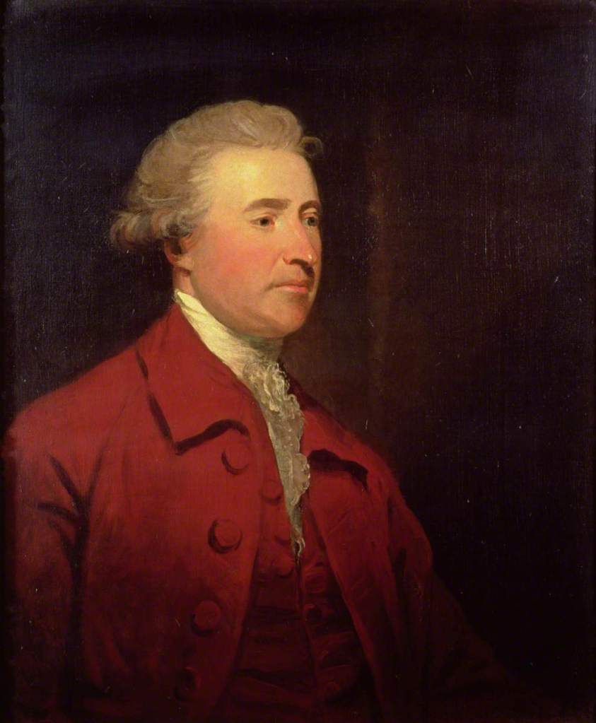 Painting of Edmund Burke. He is sat facing to the left of the canvas. He has short grey hair curled up at his ears, a long nose and rosy cheeks. He wears a whiter shirt with ruffled collar, red waistcoat and matching red jacket. 