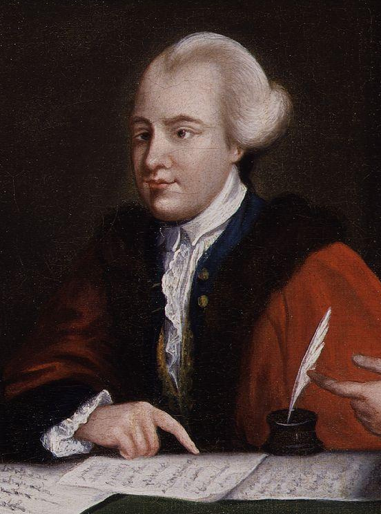 Portrait of John Wilkes. He is sat at a table, pointing to a series of hand written papers in front of him. A quill and ink pot also sits on the table. He has short grey hair and a high foreheard. He is wearing a white shirt and blue waistcoat under a red coat trimmed with brown fur collar and cuffs.